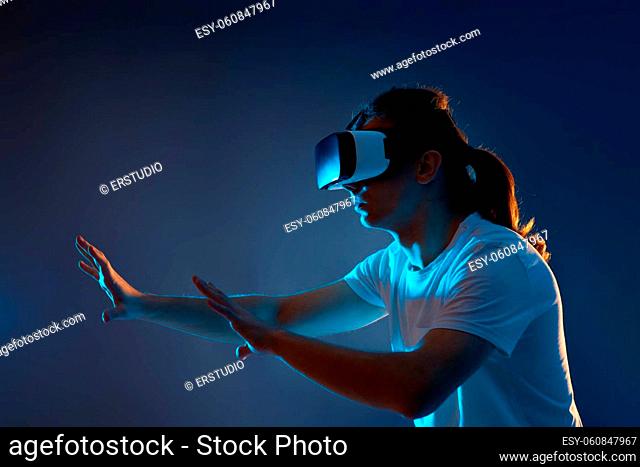 Young man wearing virtual reality goggles on dark blue background. Neon light