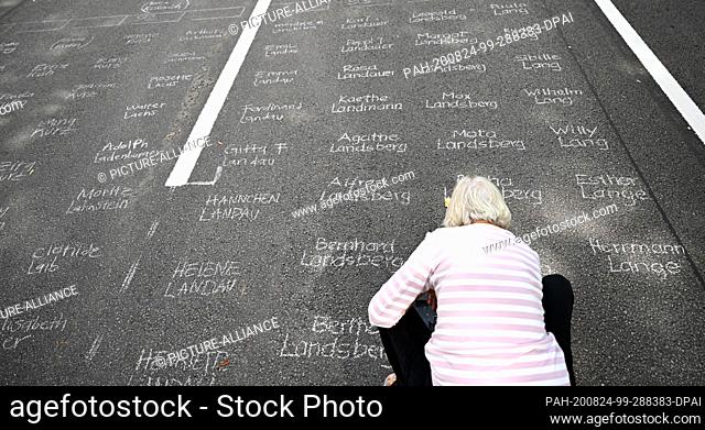 24 August 2020, Hessen, Frankfurt/Main: Christine Madelung from Frankfurt writes names on the street with white school chalk at the art action ""Writing against...