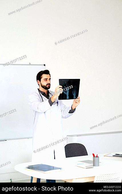 Male doctor analyzing X-ray report while standing at desk in hospital