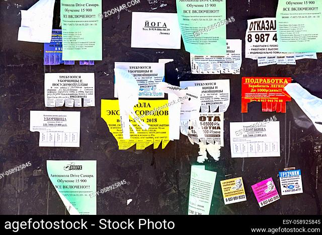 Samara, Russia - May 5, 2018: Live bulletin board. Paper ads on the wall. Shreds of various ads on an old wooden wall