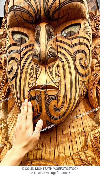 Maori carving, a tourist's hand feels texture of face, Rotorua, New Zealand