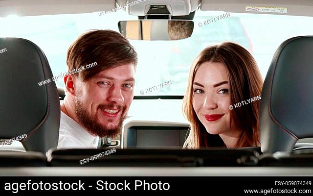 Attractive caucasian couple turning their faces to the back seat inside the car. Handsome man and pretty woman sitting on front seats