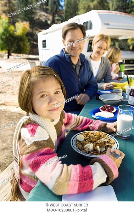 Girl eating at picnic table with family in campground
