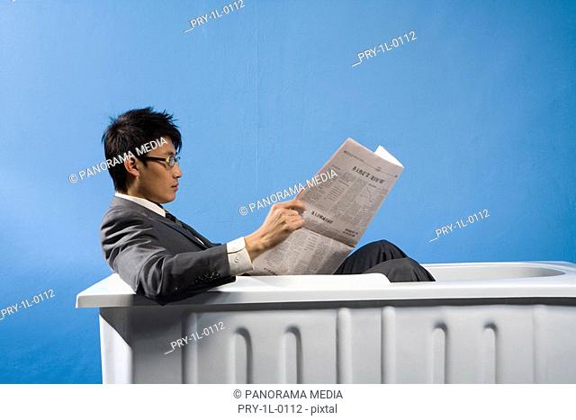 a business man sitting in the bath and reading the newspaper