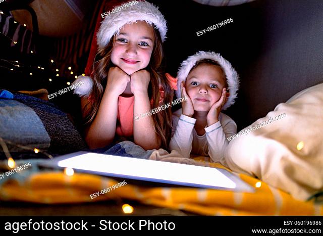 Happy caucasian siblings wearing santa hats and using tablet at christmas time