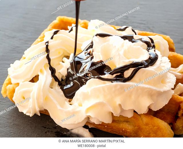 Chocolate syrup falling on a Belgian waffle with cream on a slate plate