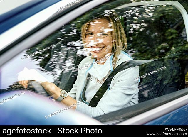 Portrait of smiling car driver with protective mask looking out of car window