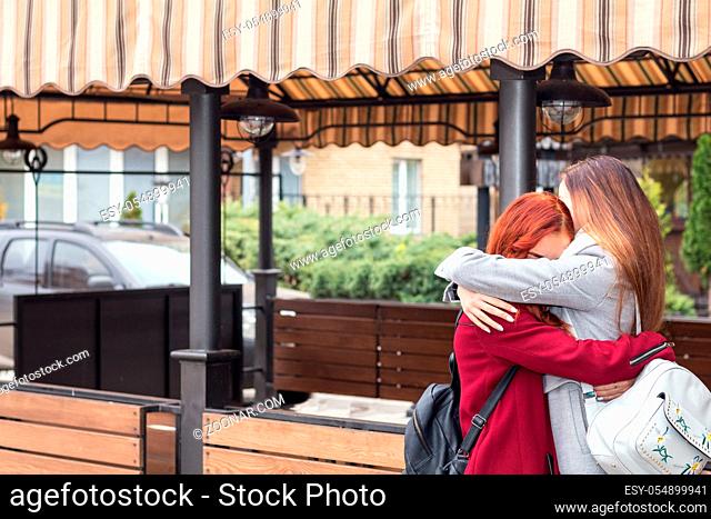 Two female teenagers embracing at the city street cafe