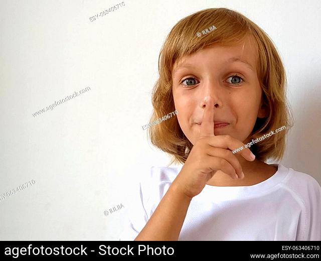 Silence gesture. The finger is near the mouth. The girl on a white background shows a gesture of keeping silence. Child of 7 years old with blond hair