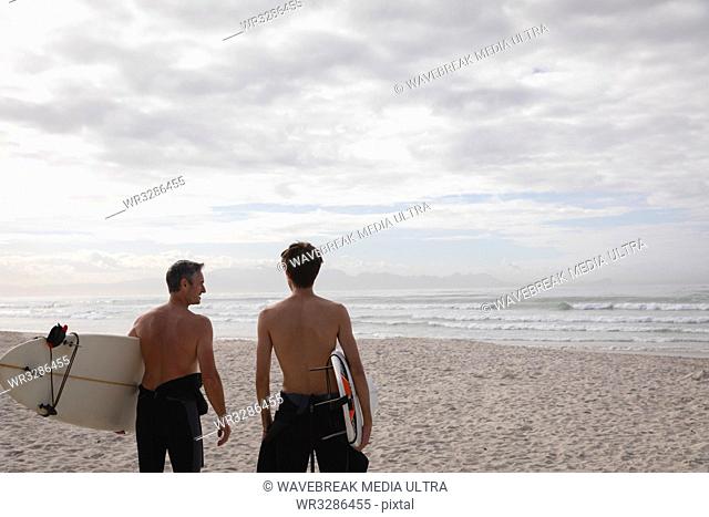 Rear view of Caucasian father and son standing with surfboard at beach