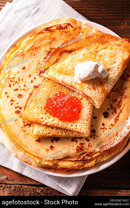 Traditional Russian Crepes Blini stacked in a plate with red caviar, fresh sour creamon dark wooden table. Maslenitsa traditional Russian festival meal