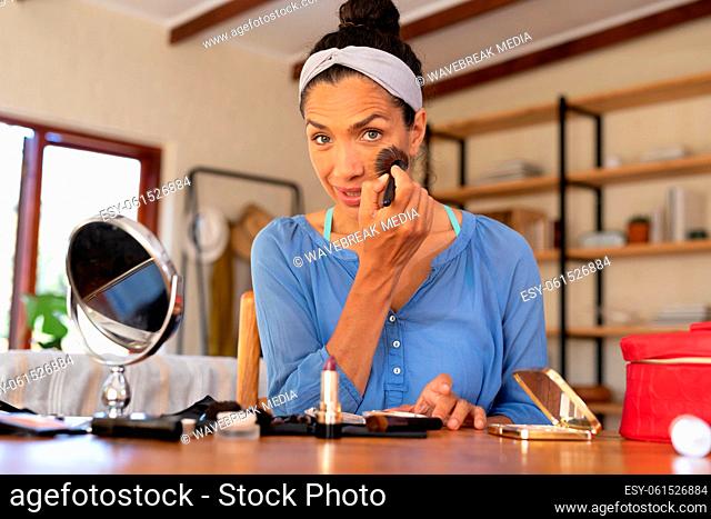 Portrait of caucasian woman applying makeup, holding makeup brush at home
