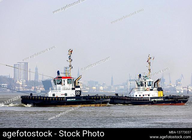 The tugs Peter and Bugsier 22 pull a large container ship in the port of Hamburg in front of the Burchardkai