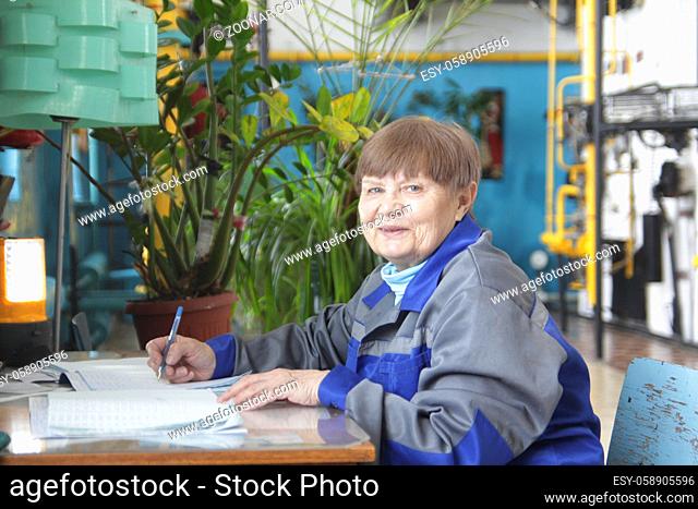 Elderly woman in workwear is writing on workplace, close up
