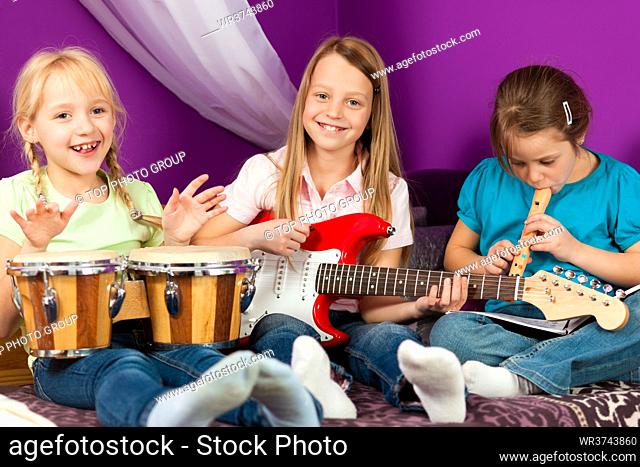 Children - sisters - making music, they are practicing playing guitar, bongo and flute
