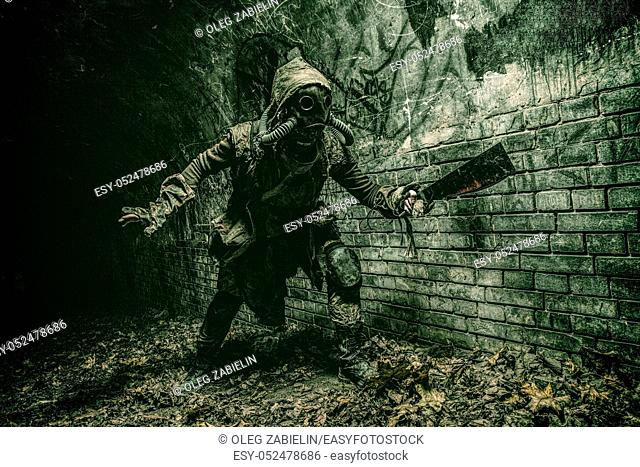 Post apocalyptic mutant creature or survivor in tatters and gas mask jumps out of darkness and attacking with handmade machete in abandoned tunnel