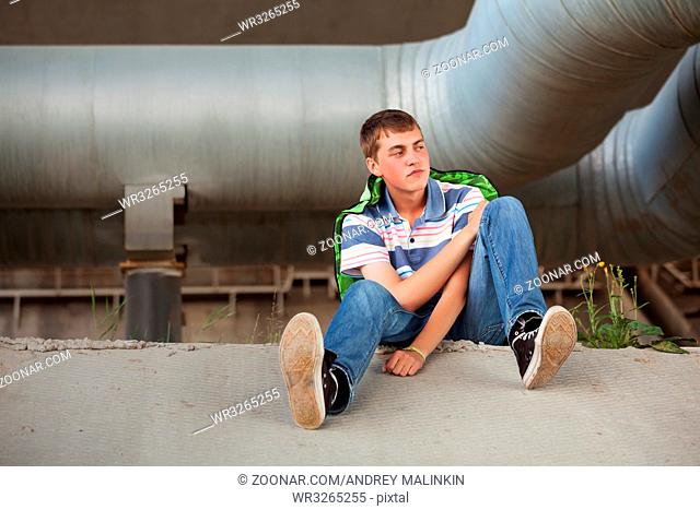Sad teen boy in depression sitting on the ground outdoor