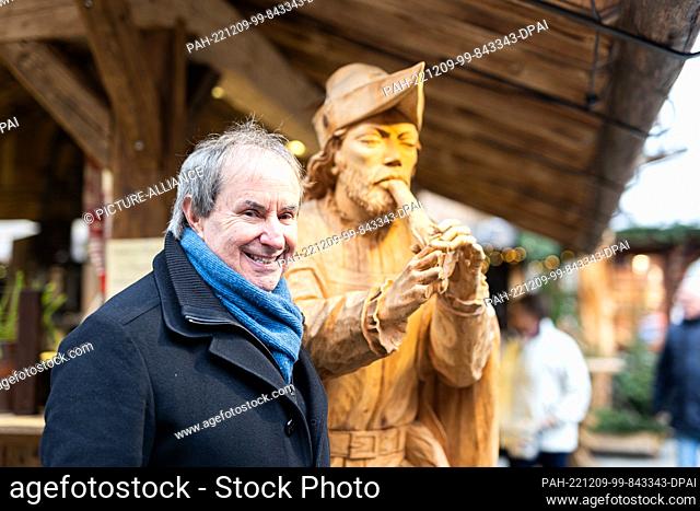 09 December 2022, Lower Saxony, Hameln: Chris de Burgh, singer and composer, stands in front of a wooden figure of the legendary figure ""The Pied Piper of...
