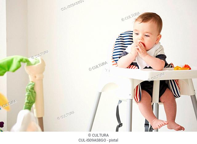 Baby boy feeding himself in baby chair