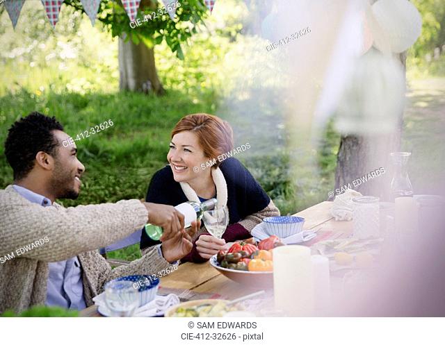 Smiling couple pouring wine at garden party table