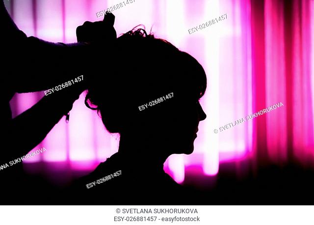 Silhouette of a female head and a hairdresser hands on a background of purple curtains