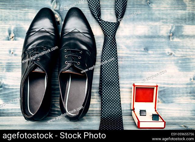 Black leather men's shoes with cufflinks in a red and white box with a polka dot tie on a wooden texture. High quality photo