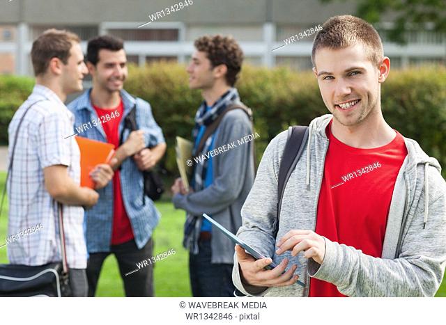 Happy male student using his tablet in front of his classmates outside