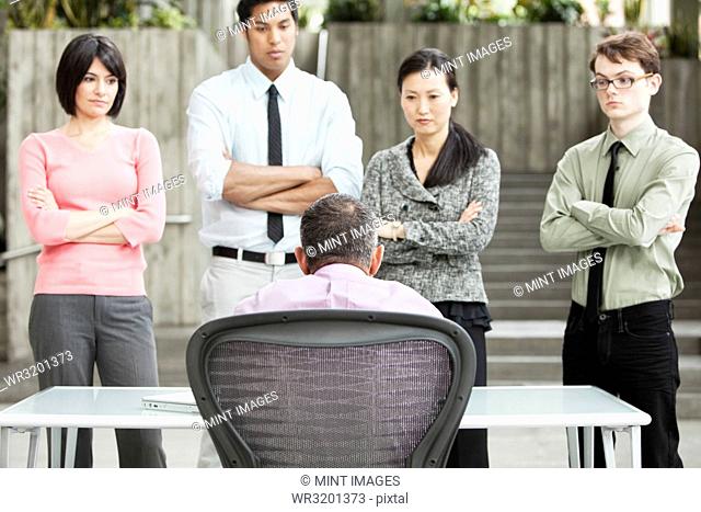 A mixed race group of business people standing in front of a person at a desk