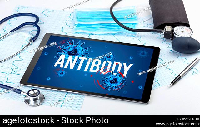 Tablet pc and doctor tools on white surface with ANTIBODY inscription, pandemic concept