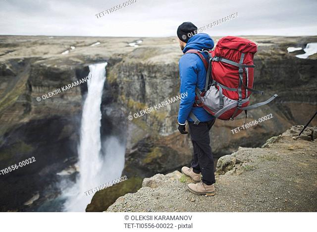 Hiker with backpack on cliff by Haifoss waterfall in Iceland