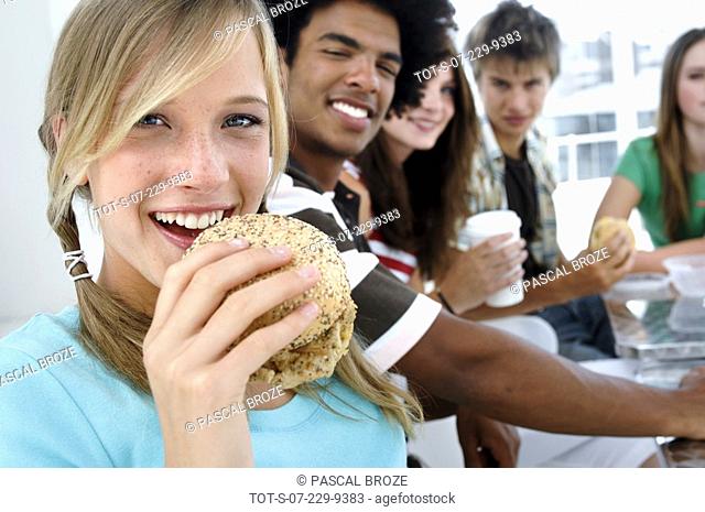 Portrait of a teenage girl eating a burger with her friends sitting behind her