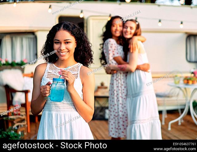 Beautiful african american female portrait during picnic beside her camper van and friends on background. Vacation, trip and holiday concept