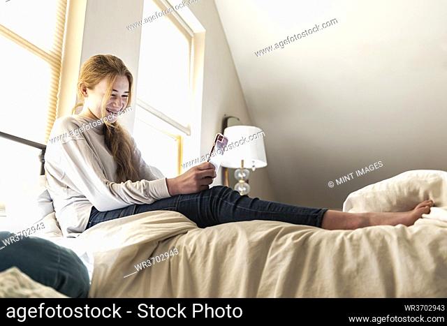 teenage girl lying on her bed using her smart phone