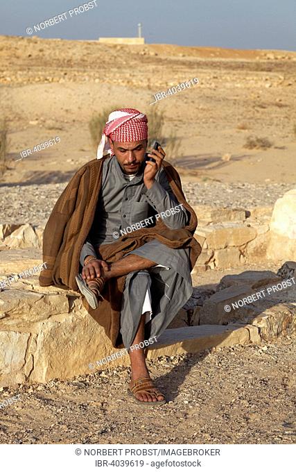 Jordanian in traditional dress on a mobile phone, desert castle Qasr Amra or Qusaie Amra, Jordan