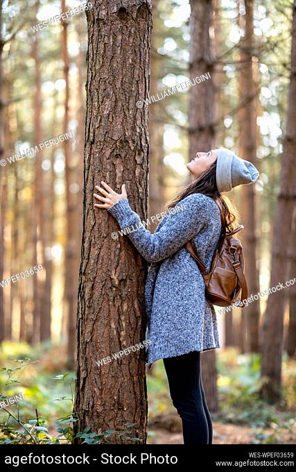 Woman looking at tree trunk while standing in Cannock Chase woodland during winter