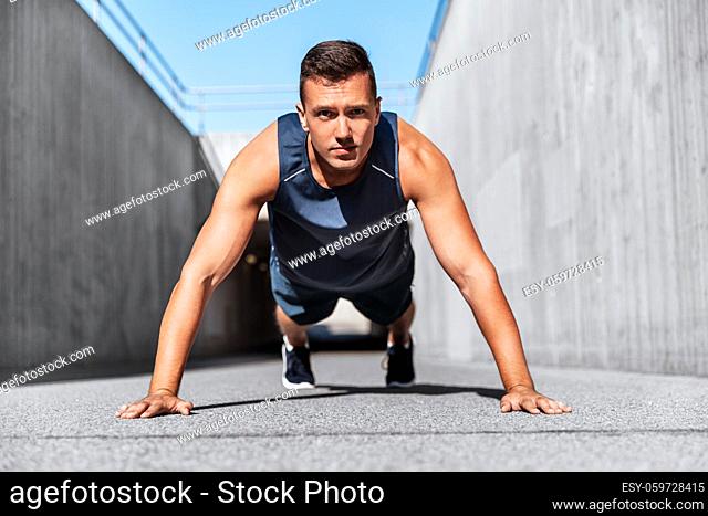 young man doing push ups on city street