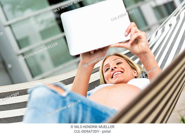 Full term pregnancy young woman lying in hammock using digital tablet