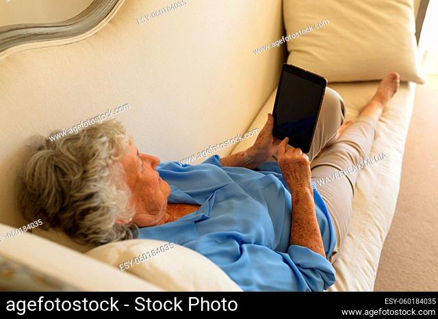 Senior caucasian woman lying on sofa and using tablet