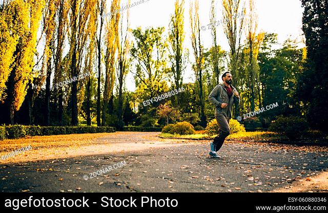 Man running in morning sunshine. Male doing cardio training in the city park
