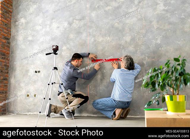 Woman and man measuring construction laser level on gray wall
