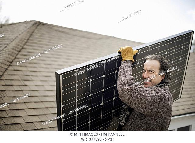 A man carrying a large solar panel across a farmyard