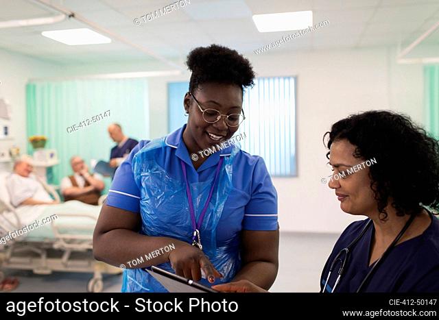 Female doctor and nurse with digital tablet making rounds, consulting in hospital room