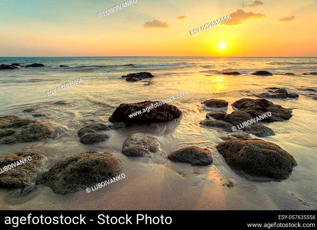 Wet sand on empty beach in golden sunset light during low tide showing rocks covered with sea algae. Kantiang Bay, Ko Lanta, Thailand