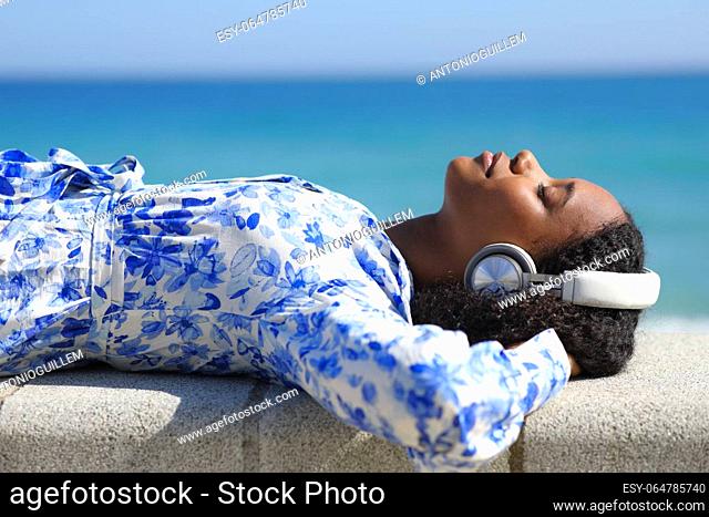 Profile of a black woman wearing headphone relaxing listening music on the beach
