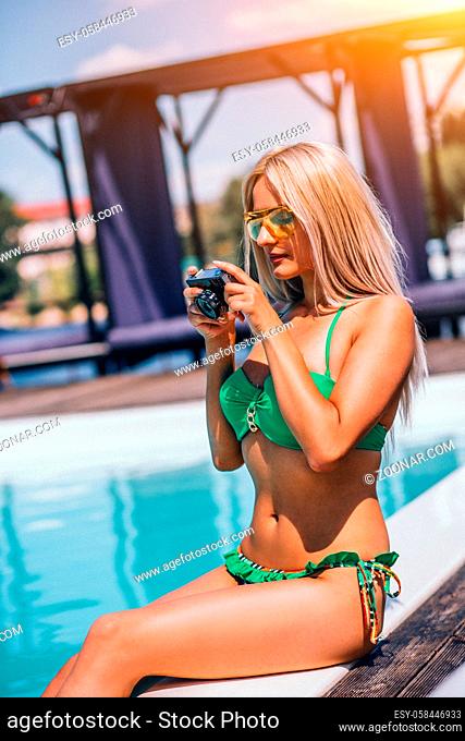 Young Blondie Woman In Green Bikini Is Relaxing Near Swimming Pool And Watching Photos On The Camera.She Is wearing Glasses