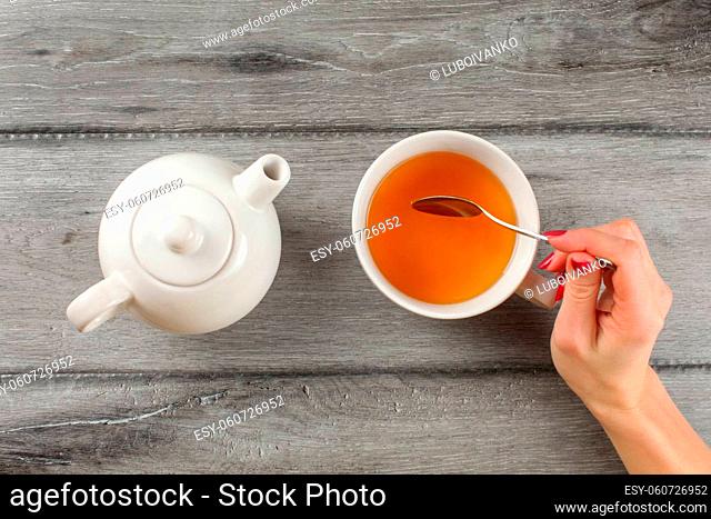 Table top view - woman hand holding spoon, stirring tea in white porcelain cup