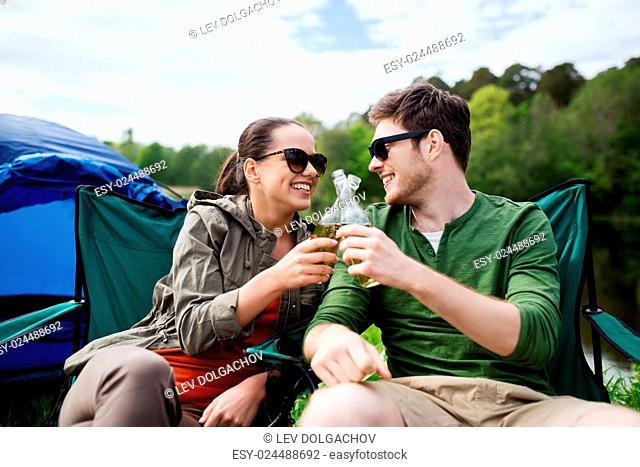 camping, travel, tourism, hike and people concept - happy friends clinking glass bottles and drinking cider or beer at campsite