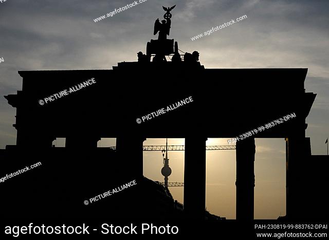 19 August 2023, Berlin: The Brandenburg Gate and the TV Tower can be seen in the backlight of the rising sun. People in Berlin and Brandenburg have to prepare...