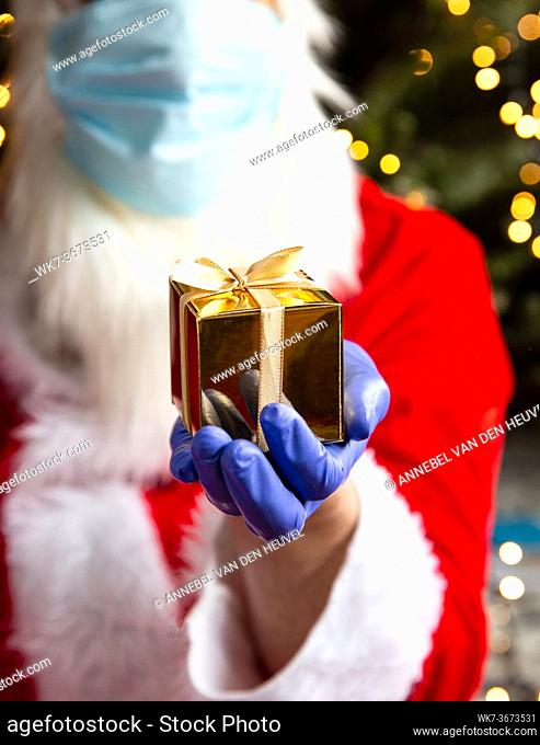 Santa Claus is holding a golden gift box wearing protective gloves and a Safety mask for Coronavirus, Covid-19 and Christmas concept present
