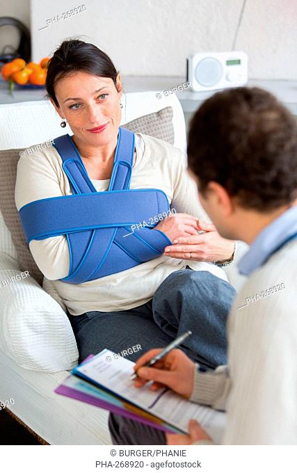 Doctor visiting female patient wearing a splint, at home